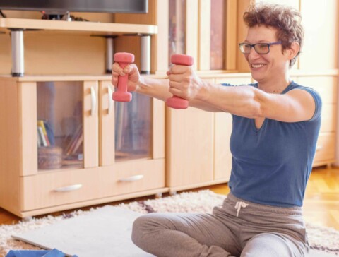 Young caucasian female adult exercising at home while sitting on the floor and strechting her arms