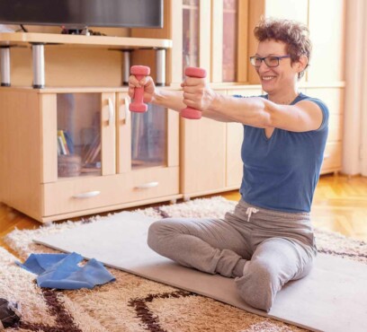Young caucasian female adult exercising at home while sitting on the floor and strechting her arms