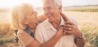 Senior caucasian adult couple smiling and holding each other in a field.