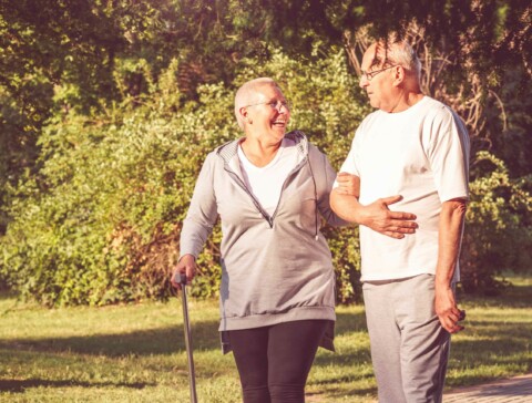 Mature caucasian female patient with a cane, taking a walk in a park while holding her husband