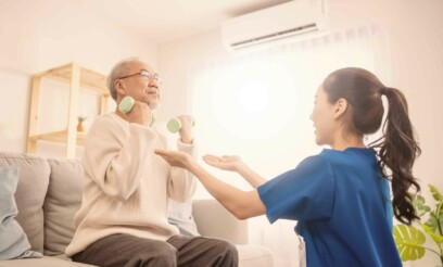 Senior asian male patient exercising at home and stretching his arms with the help of an asian young female physiotherapist