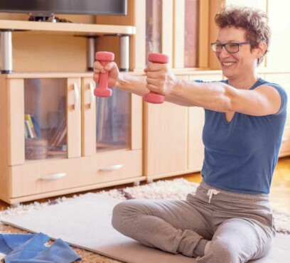 Young caucasian female adult exercising at home while sitting on the floor and strechting her arms