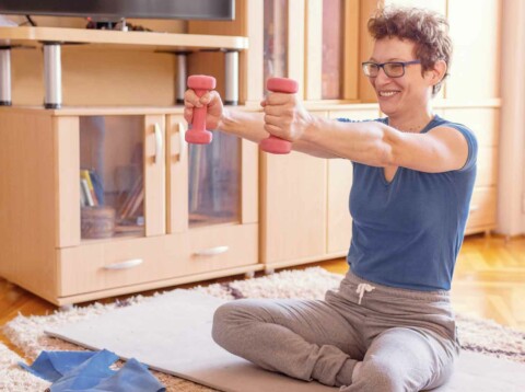 Young caucasian female adult exercising at home while sitting on the floor and strechting her arms
